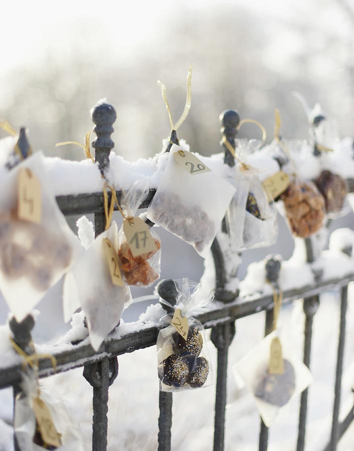 Small Bags Of Biscuits Hanging On Snowy Fence As Advent Calender #1 Photograph by Hannah Kompanik