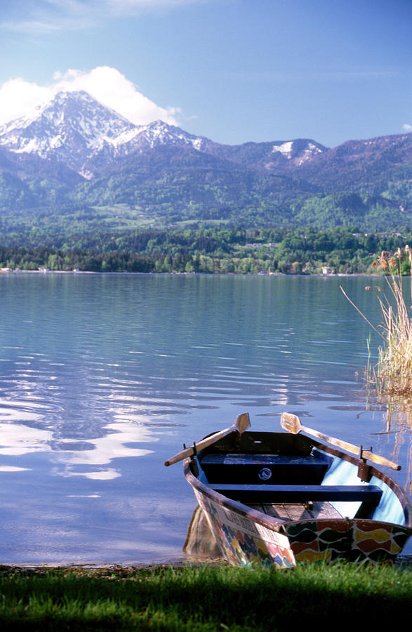 View Of Mountains Overlooking Boat Moored Near Shore Of Lake Worth, Austria #1 Photograph by Jalag / Matteo Manduzio