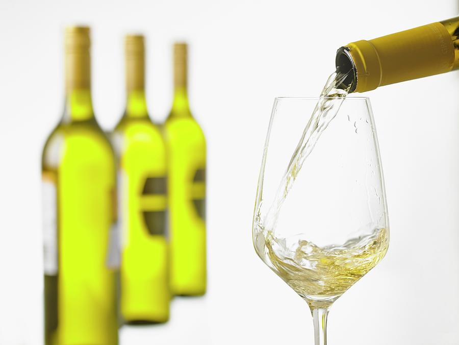 White White Being Poured Into A Glass With A Row Of Wine Bottles In The Background #1 Photograph by Foto4food