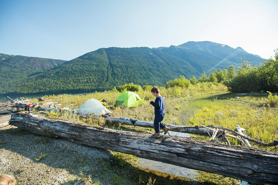 Sunset Photograph - Young Boy Balancing On Fallen Log Near Wilderness Campsite, Canada. #1 by Cavan Images