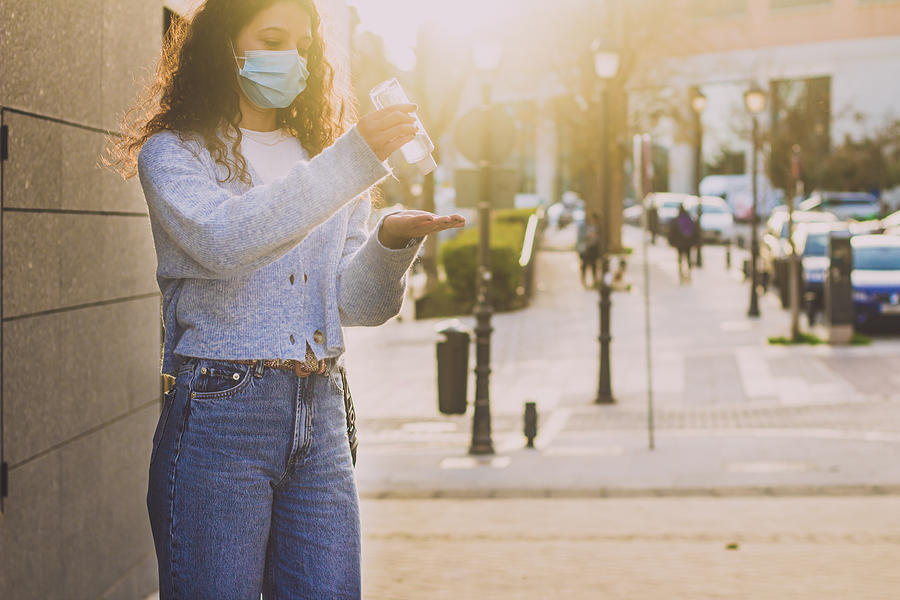 Sunset Photograph - Young Woman Applying Sanitizer Gel On Her Hands In The Street #3 by Cavan Images