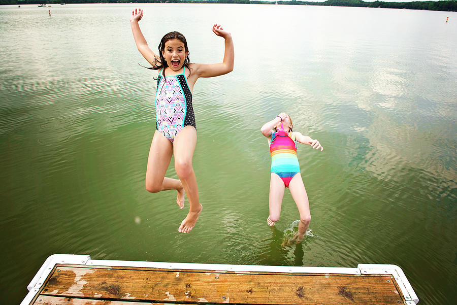 Two Young Girls In Swimsuits Jumping Off A Dock Into A Lake Photograph