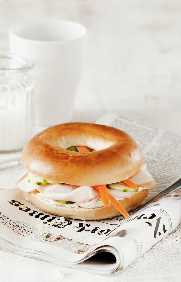 A Bagel With Turkey Breast And Carrots On A Newspaper Photograph by Birgit Twellmann