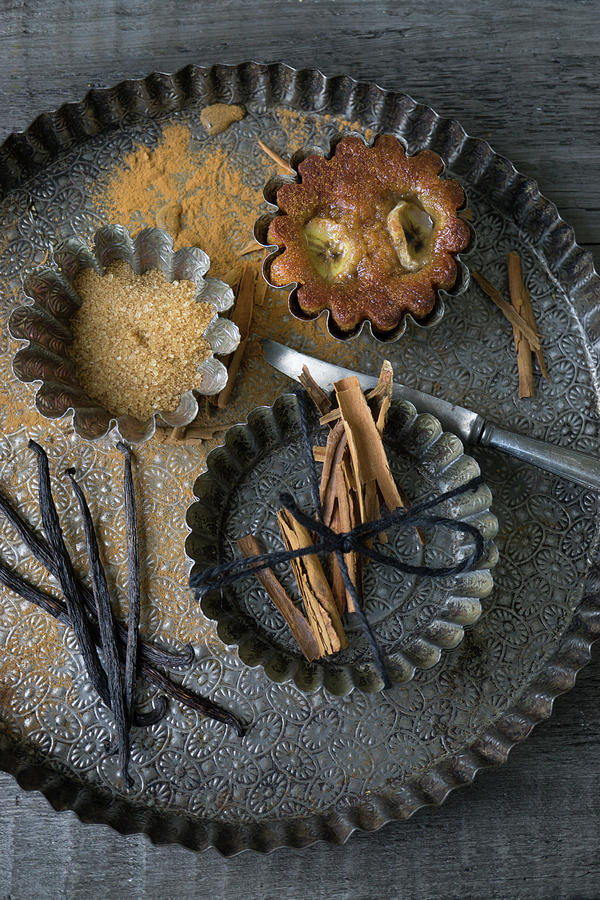 A Banana Muffin In A Tin Next To Cinnamon, Sugar And Vanilla Photograph by Martina Schindler