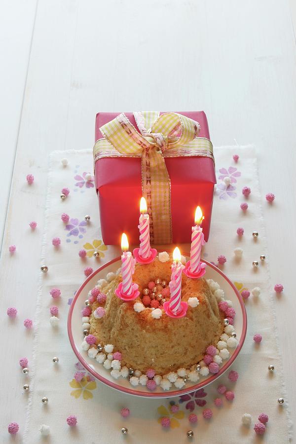 A Birthday Cake With Four Burning Candles And A Gift-wrapped Present With A Bow Photograph by Regina Hippel