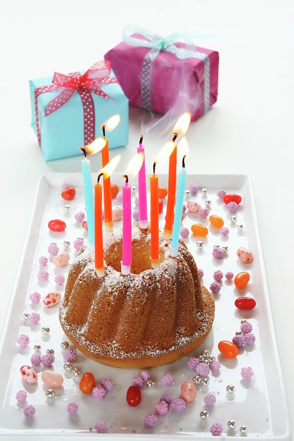 A Birthday Cake With Lit Candles Being Blown Out, And Wrapped Presents Photograph by Regina Hippel