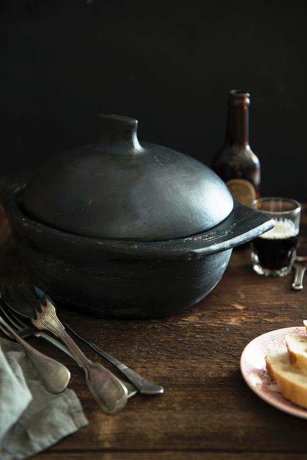 A Black Cooking Pot, Silver Cutlery, Bread And Beer On A Wooden Table england Photograph by Veronika Studer