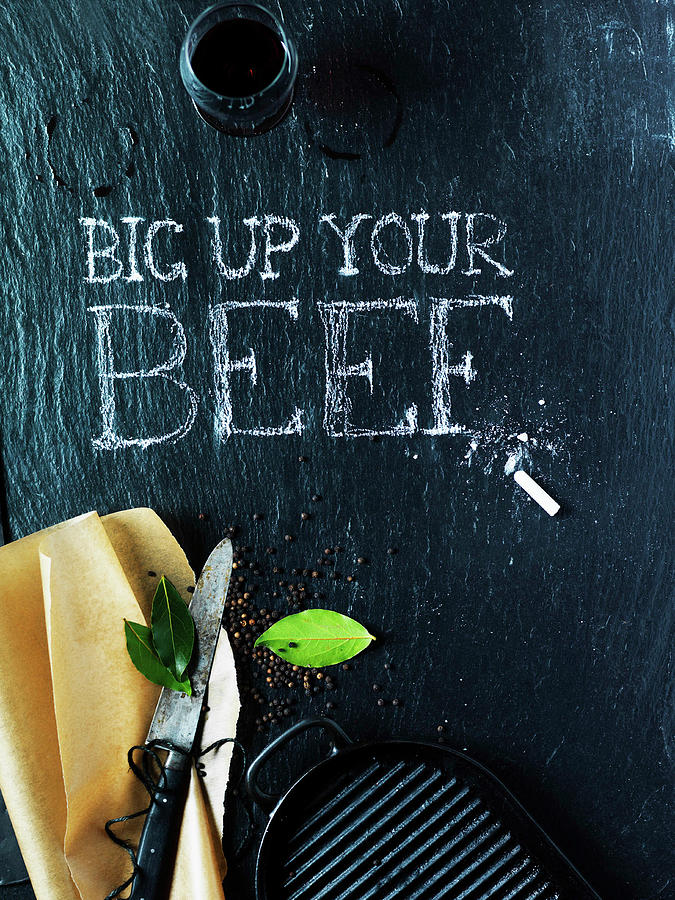 A Blackboard Wtih big Up Your Beef Written In Chalk, A Knife, Bay Leaf, A Griddle, And Black Pepper Photograph by Karen Thomas