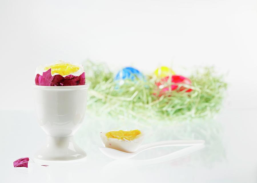 A Boiled Egg With The Top Cut Off, In An Eggcup, With An Easter Nest Of Colourful Eggs In The Background Photograph by Foto4food