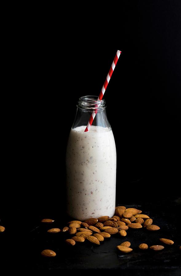 A Bottle Of Almond Milk And Almond Is On A Black Surface Photograph by Hein Van Tonder