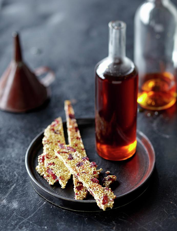 A Bottle Of Caramel Syrup And Sesame Brittle With Cranberries Photograph by Jalag / Janne Peters