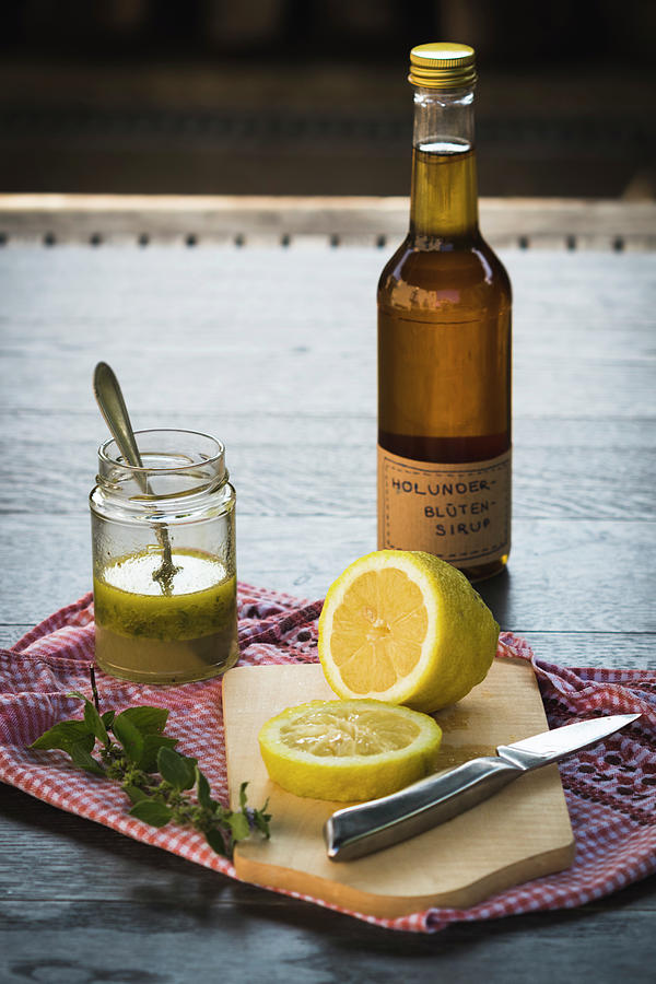 A Bottle Of Elderflower Syrup Behind A Sliced Lemon On A Wooden Surface Photograph by Antonia Kurz