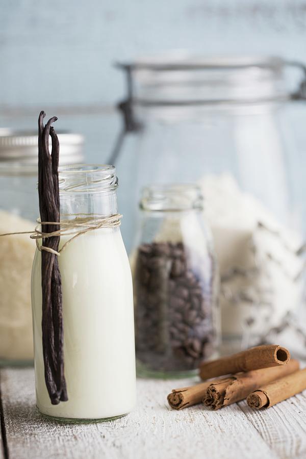 A Bottle Of Milk With Vanilla Pods, Cinnamon Sticks, Coffee Beans, Cane Sugar And Cutters Photograph by Tina Engel