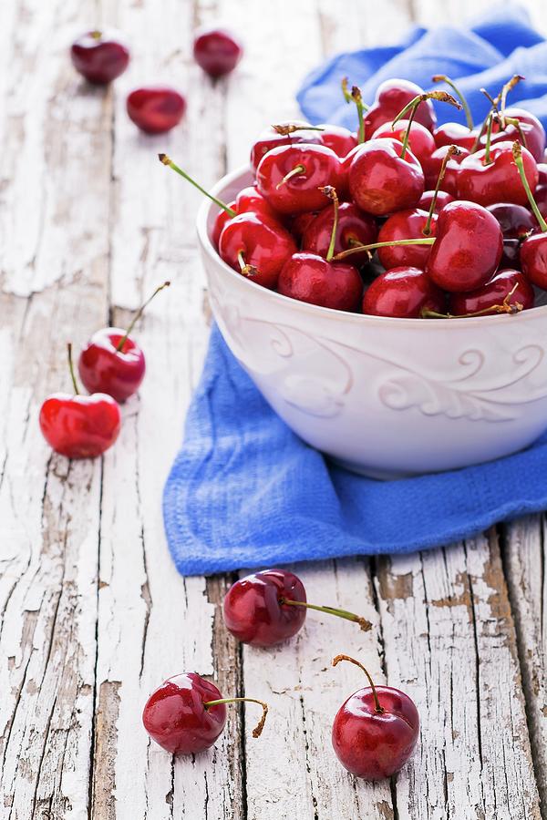 A Bowl Of Fresh Cherries On A Blue Cloth On A Weathered Wooden Table Photograph by Brian Enright