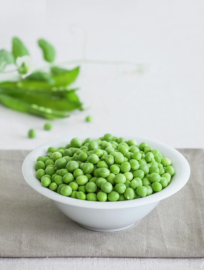 A Bowl Of Fresh Peas With Pea Pods In The Background Photograph by Matteo Mezzadri