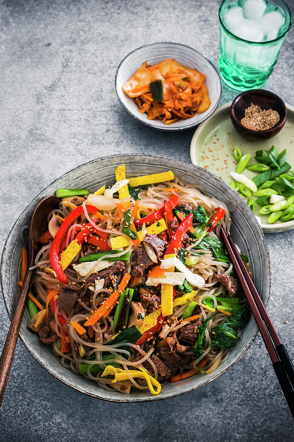 A Bowl Of Korean Glass Noodles Stir-fried With Vegetables, Topped With Toasted Sesame Seed And Garnished With Spring Onions And Kimchi Photograph by Maricruz Avalos Flores