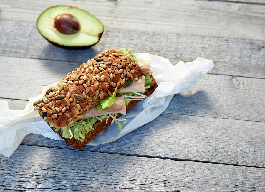 A Bread Roll With Smoked Trout, Sprouts And Avocado On Paper Photograph by Stefan Schulte-ladbeck