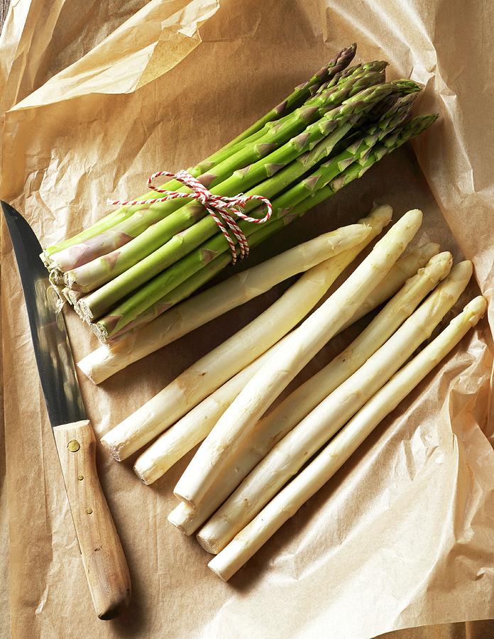 A Bunch Of Green Asparagus And Loose White Asparagus On A Piece Of Paper With A Knife Photograph by Ludger Rose