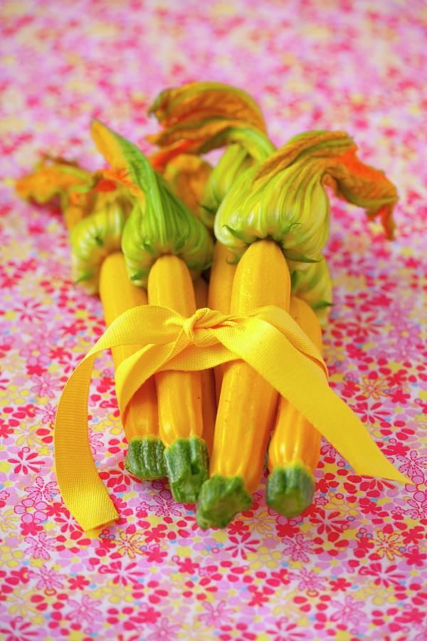 A Bunch Of Yellow Courgettes With Flowers Tied Together With A Ribbon On A Floral Tablecloth Photograph by Studio Lipov
