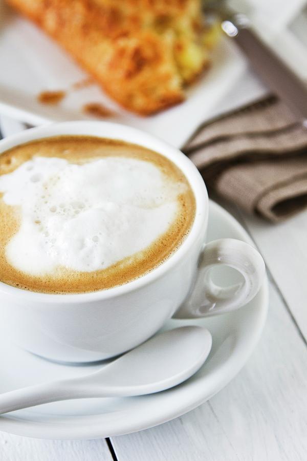 A Cappuccino With Milk Foam And An Apple Turnover In The Background Photograph by Catja Vedder