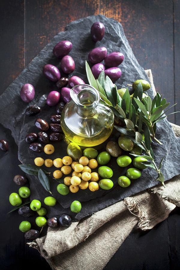 A Carafe Of Olive Oil, Various Olives And An Olive Spring On A Stone Platter Photograph by Malgorzata Stepien
