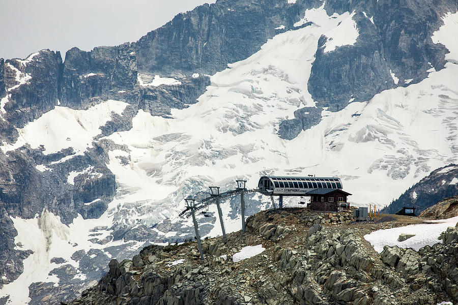 Mountain Photograph - A Chairlift Comes To The Top Of A Mountain Backdropped By A Glaciated Peak Behind In The Coast Mountains Of British Columbia. by Cavan Images