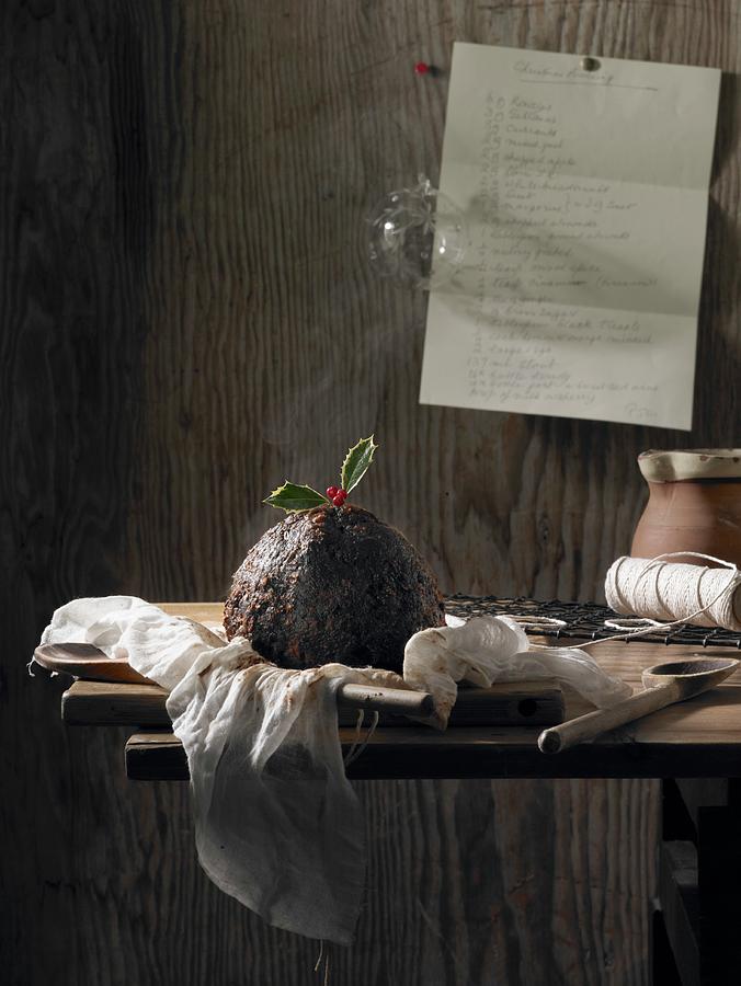 A Christmas Pudding Decorated With Holly On A Rustic Wooden Table With A Hand-written Recipe Pinned To The Wall Behind Photograph by Atkinson / Sue Dr.