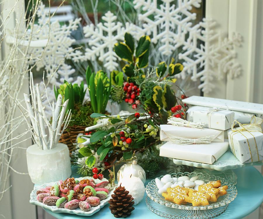 A Christmas Table Laid With Flowers, Presents, Candles And Biscuits In Front Of A Window Decorated With Snowflakes Photograph by Linda Burgess