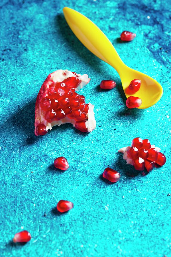 A Chunk Of Pomegranate And Pomegranate Seeds On A Turquoise Surface With A Yellow Spoon Photograph by Mandy Reschke