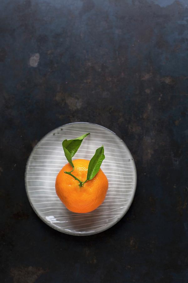 A Clementine With Leaves On A Plate On A Dark Surface Photograph by Tina Engel