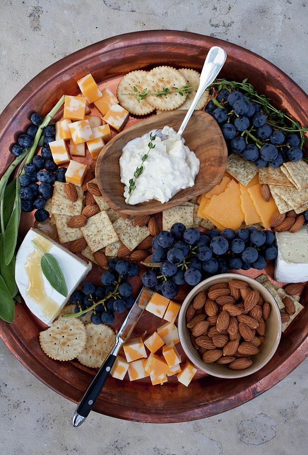 A Copper Tray On A Stone Surface, With Marbled Cheddar Cheese Cubes, Concord Grapes, Blueberries, Crackers, Brie Topped With Honey And Sage, Artichoke Dip With Thyme, Almonds And A Sprig Of Sage Photograph by Ryla Campbell