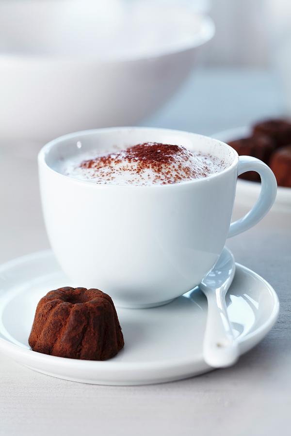 A Cup Of Cappuccino And A Praline In The Shape Of A Ring Cake Photograph by Taube, Franziska