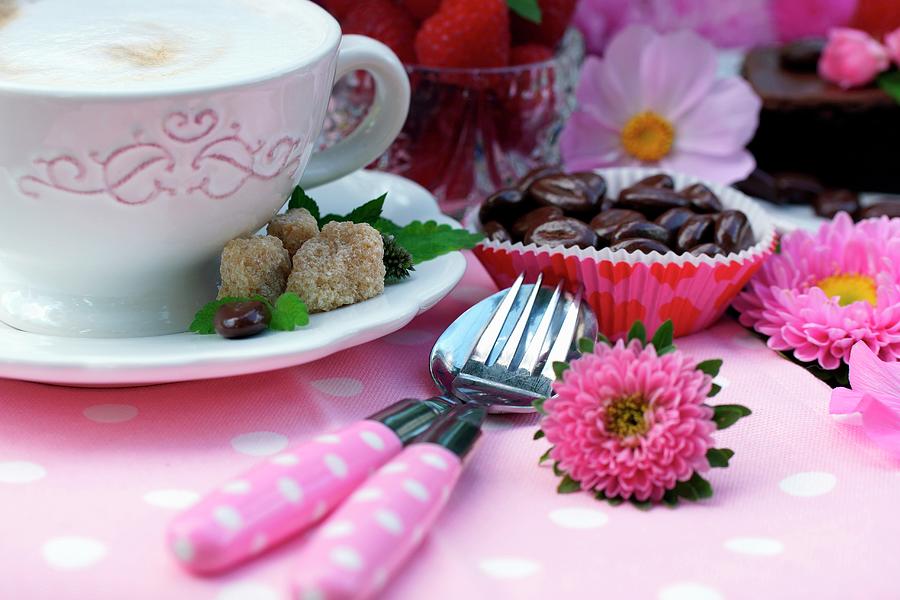A Cup Of Cappuccino Next To Dessert Cutlery And Coffee Beans In Paper Cases On A Decorated Garden Table Photograph by Angelica Linnhoff