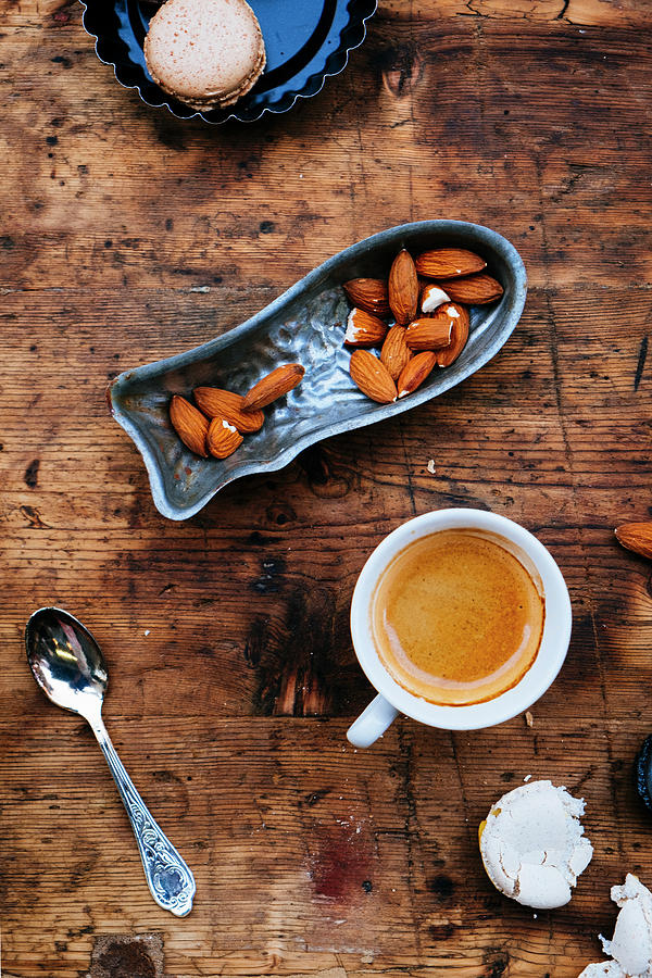 A Cup Of Coffee With A Brown Macaron And Almond Nuts On A Wooden Table Photograph by Lucie Beck