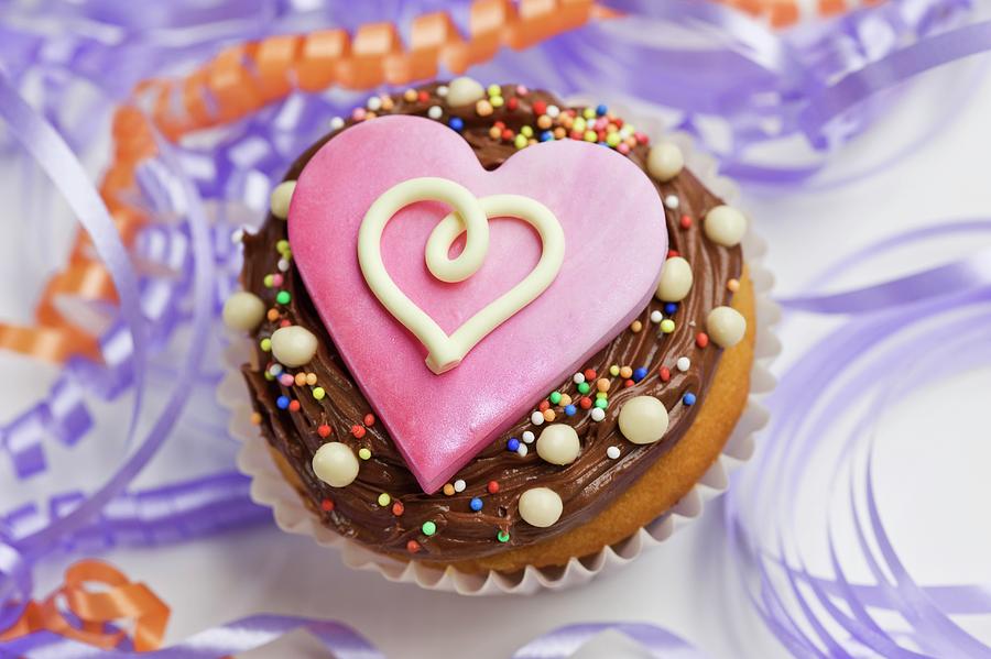 A Cupcake Decorated With Chocolate Icing And A Pink Heart Between Streamers Photograph by Linda Burgess