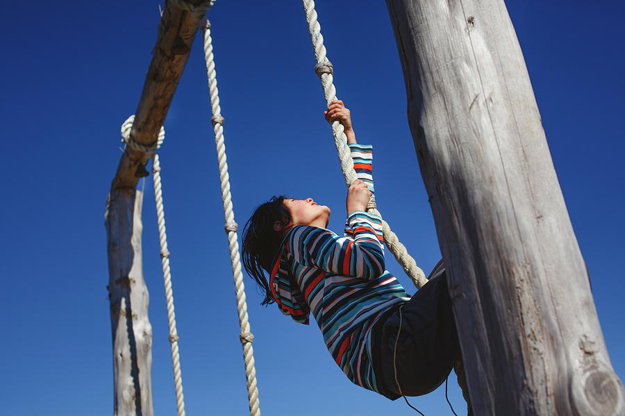 Spring Photograph - A Determined Happy Child Pulls Himself Up A Rope Against Blue Sky by Cavan Images