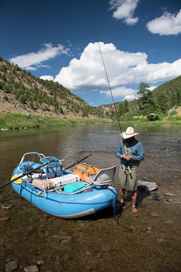 A Fly Fisherman Prepares His Gear While Standing Net To A Raft