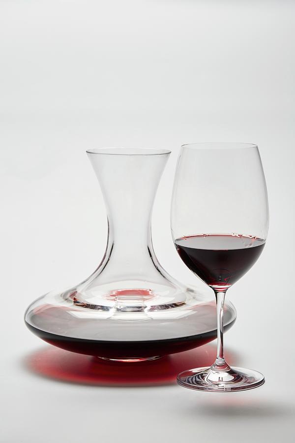 A Glass Carafe And A Glass Of Red Wine On A White Surface Photograph by Herbert Lehmann