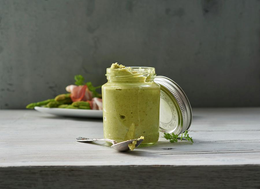 A Glass Jar Of Asparagus Pesto, With Green Asparagus And Ham In The Background Photograph by Stefan Schulte-ladbeck