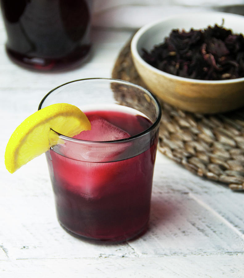 A Glass Of Cold Sorrel Drink With Lemon Wedge Garnish With Sorrel Leaves In Bowl Photograph by Jennifer Blume