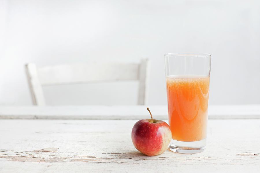 A Glass Of Fruit Juice And An Apple On A White Wooden Table With A Chair Photograph by Sabine Lscher