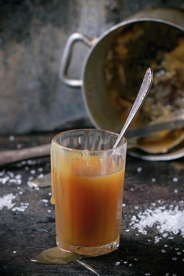 A Glass Of Homemade Caramel Sauce With An Old Pot In The Background Photograph by Natasha Breen