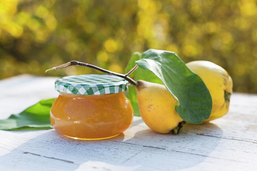 A Glass Of Homemade Quince Jam And Fresh Quinces On A Table Outdoors Photograph by Sabine Lscher