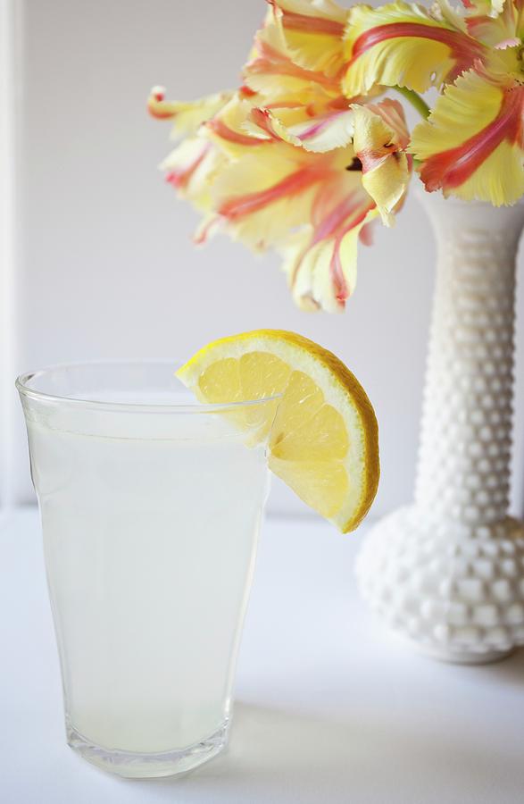 A Glass Of Lemon Water Next To A Vase Of Flowers Photograph by Ryla Campbell