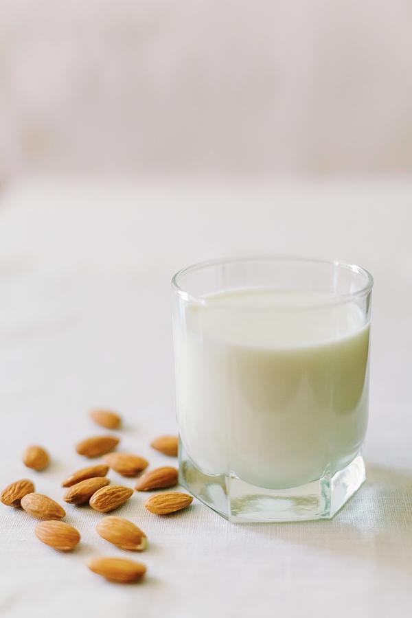 A Glass Of Milk And Almonds On A White Tablecloth Photograph by Sonya Baby