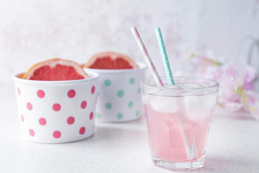 A Glass Of Pink Colored Grapefruit Infused Water With Pastel Colored Beverage Straws, Halved Grapefruit In Polka Dotted Bowls Photograph by Albina Bougartchev
