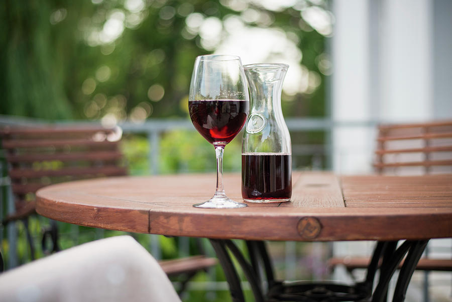 A Glass Of Red Wine And A Carafe Of Wine On A Wooden Table In A Garden Photograph by Jelena Filipinski