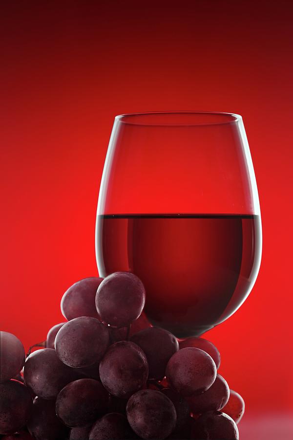 A Glass Of Red Wine And Some Red Grapes Against A Red Background Photograph by Krger & Gross