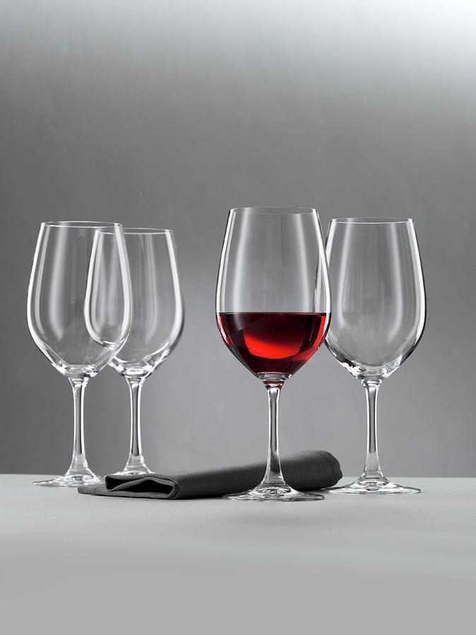 A Glass Of Red Wine And Three Empty Wine Glasses Against A Grey Background Photograph by Feig & Feig