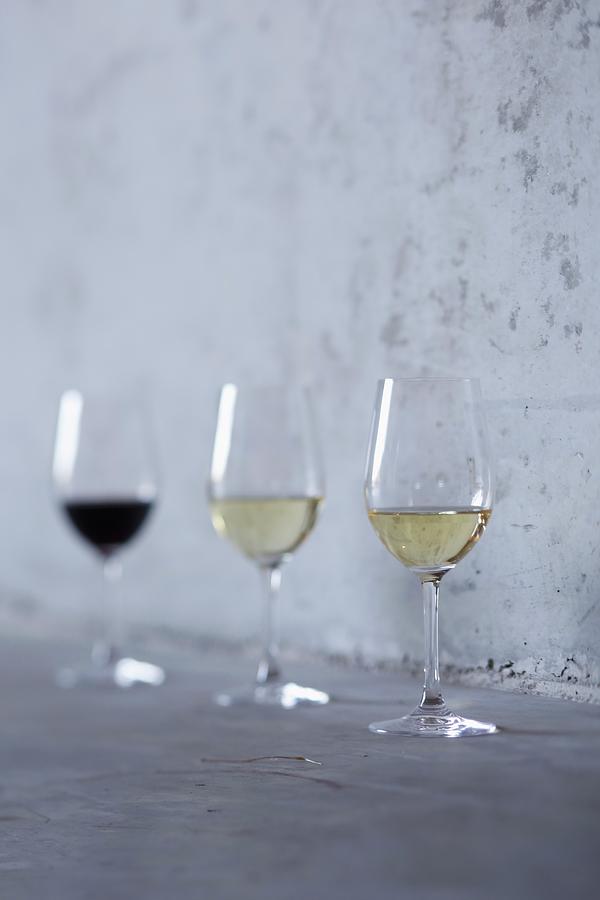 A Glass Of Red Wine And Two Glasses Of White Wine Standing Against A Stone Wall Photograph by Jalag / Markus Bassler